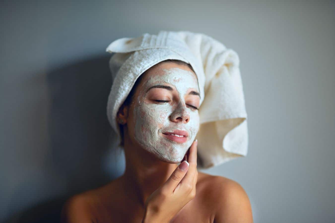 Woman with moisturizer on her face and a towel on her head.