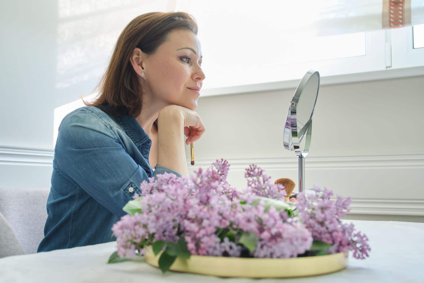 Woman examining face in the mirror for wrinkles.
