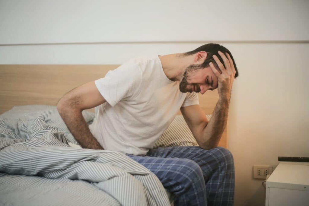 A man sitting in bed holding his head in his hand. The classic hangover posture.