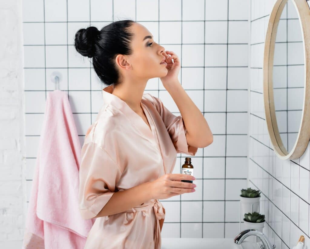 Photo of a woman at her bathroom mirror using a face cream.